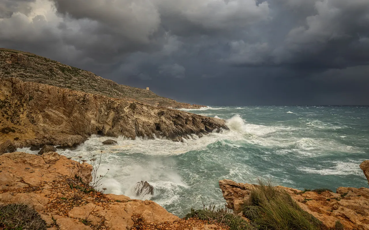 Dark storm clouds approaching over a rocky coastline with breaking waves