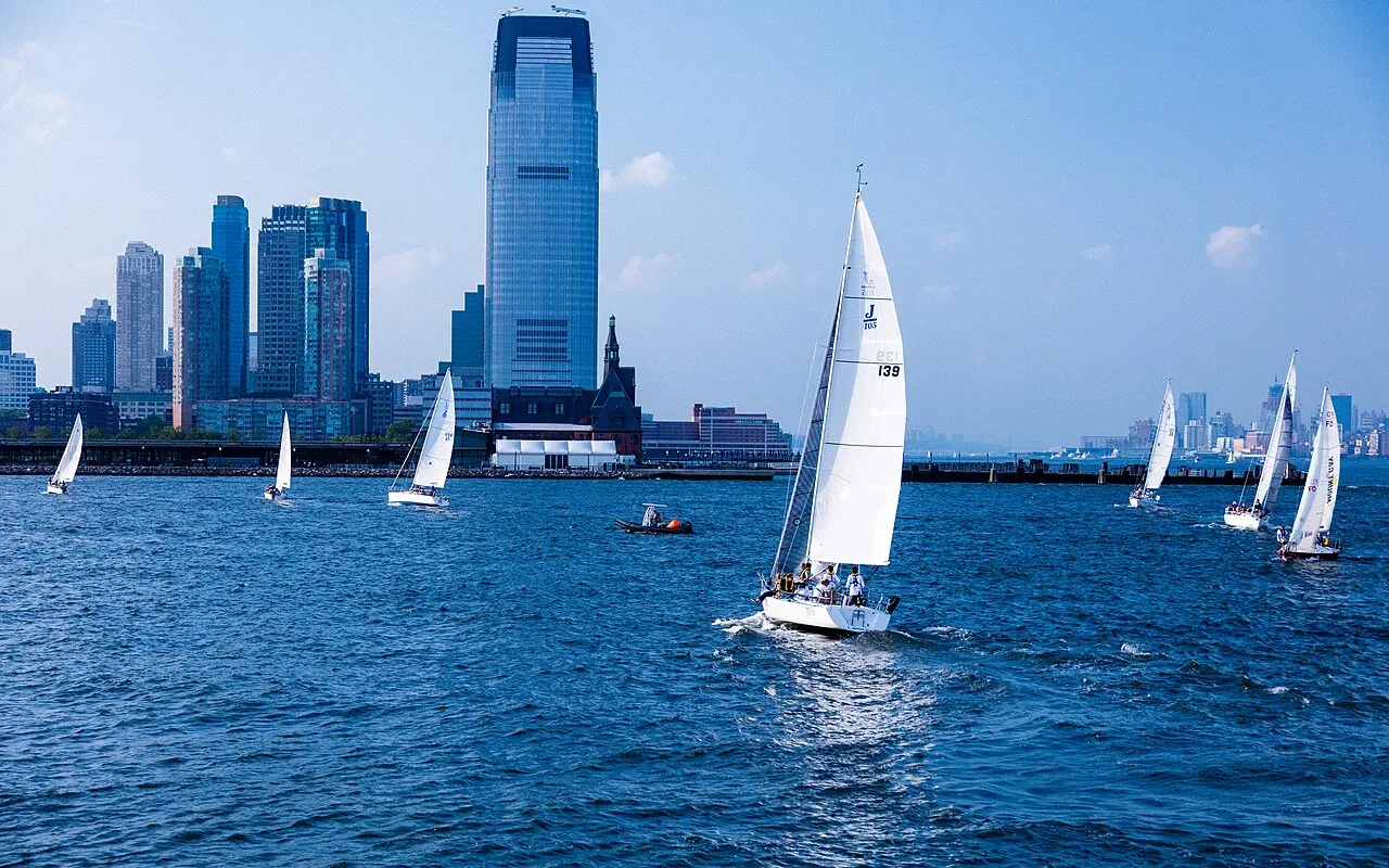 Small keelboats sailing on a harbour with a city skyline behind