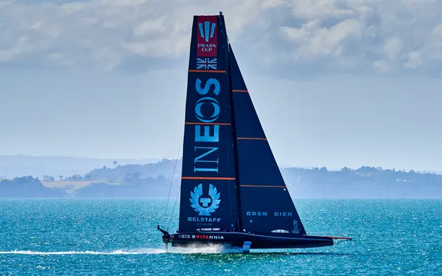 Eine AC75-Foiling-Yacht mit dunklem Rumpf und hohem schwarzem Großsegel