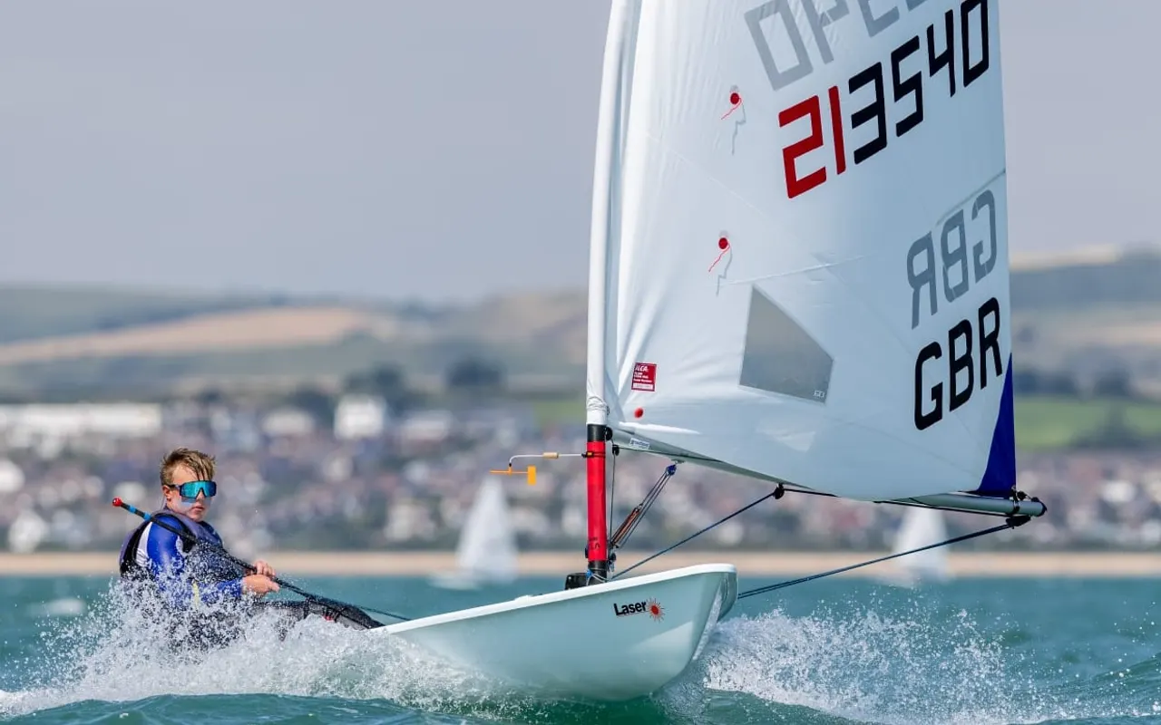 A young sailor hiking hard in an ILCA 6 dinghy in waves