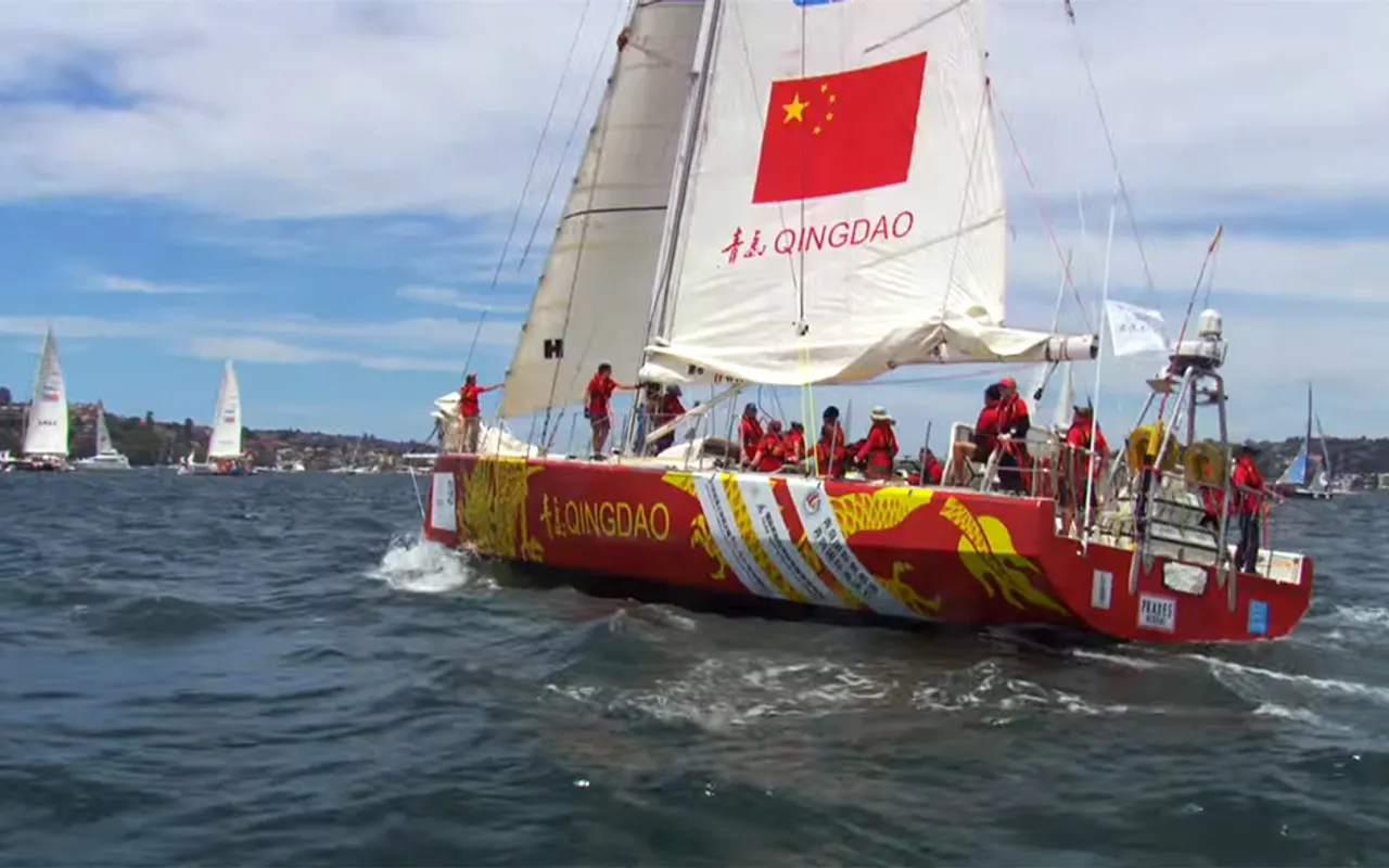 A big red and yellow offshore racing yacht with a crowded crew on the rail