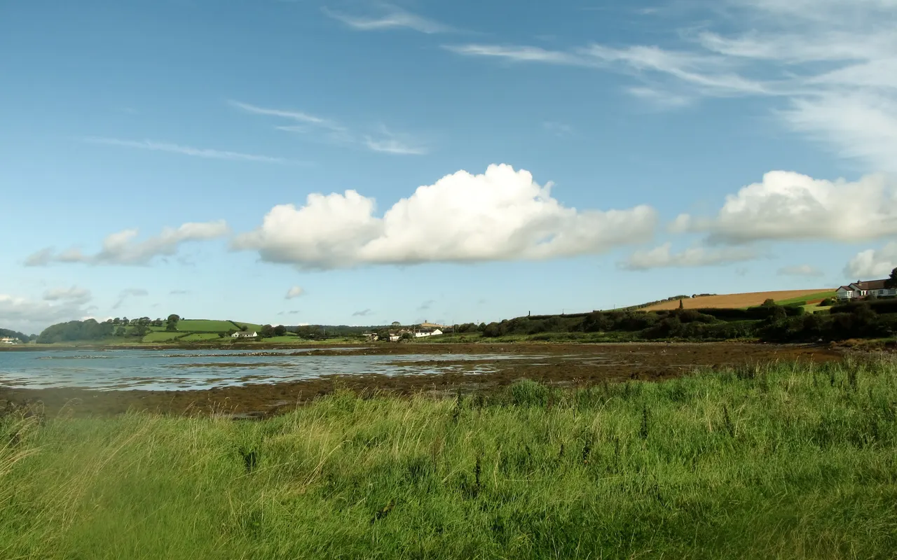 Fair-weather cumulus clouds over a green coastline and calm bay on a sunny day