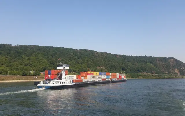 Ein langes Containerschiff auf dem Rhein zwischen bewaldeten Hügeln
