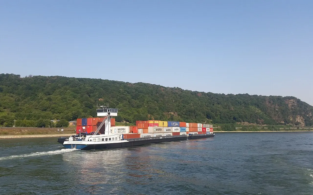 A long container barge on the Rhine between wooded hills