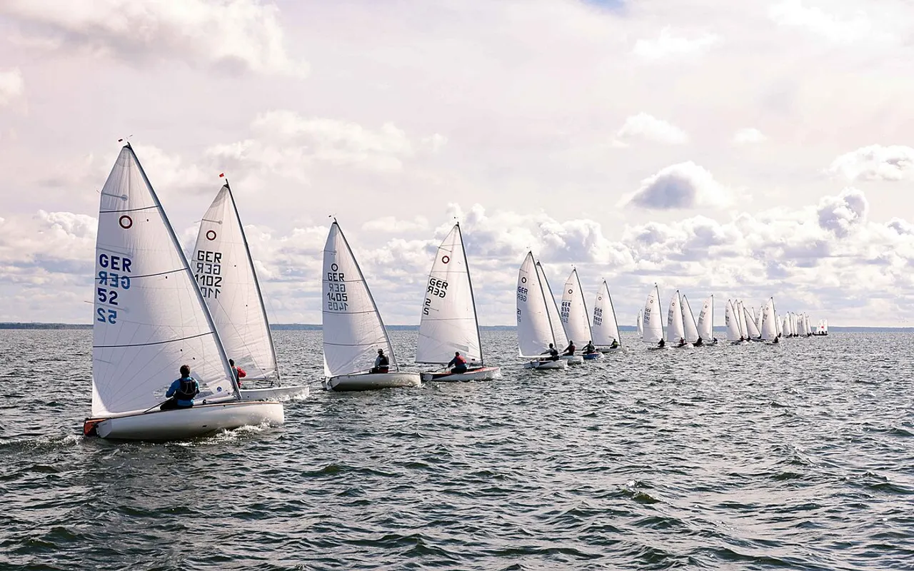 A long line of small dinghies racing in close formation on grey water