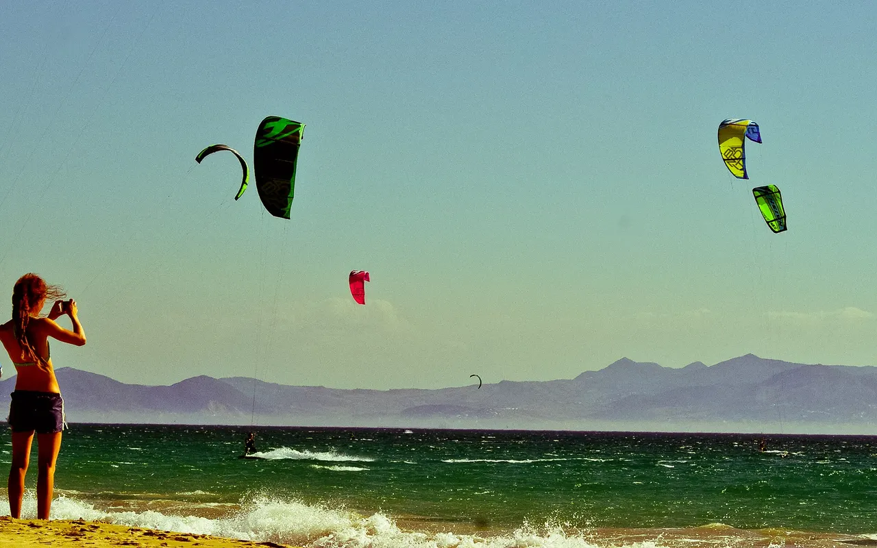 Kitesurfers on the water off a beach at Tarifa, Spain, with mountains behind