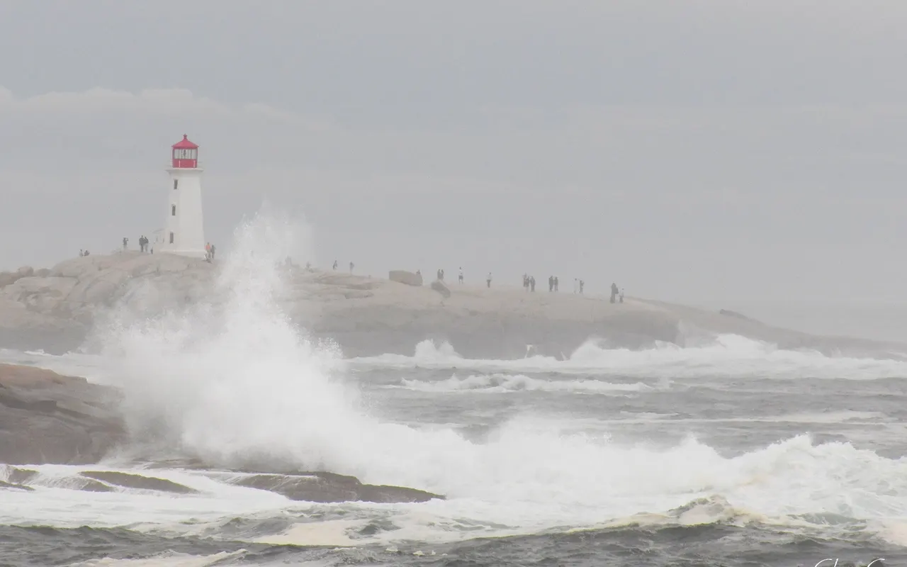 Big waves breaking on rocks below a lighthouse in a strong wind