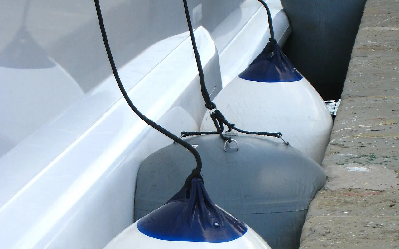 Una defensa blanca apretada entre el casco de un barco y un muelle de piedra