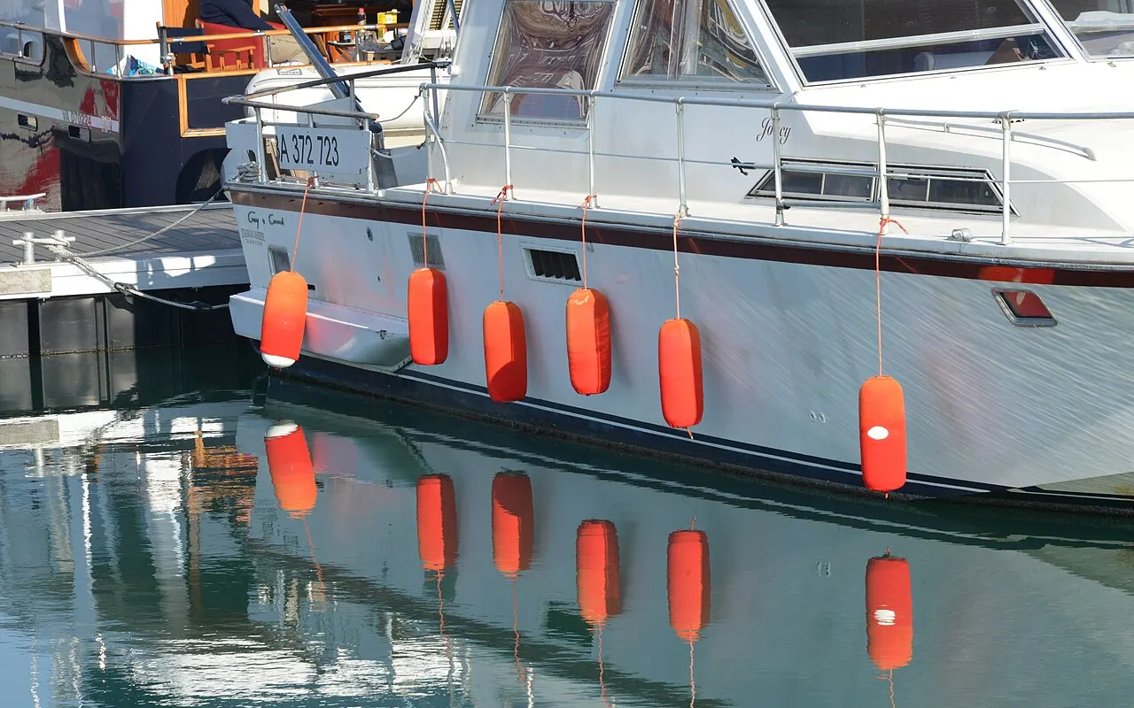 Una fila de defensas naranjas colgando uniformemente por el costado de un yate a motor blanco