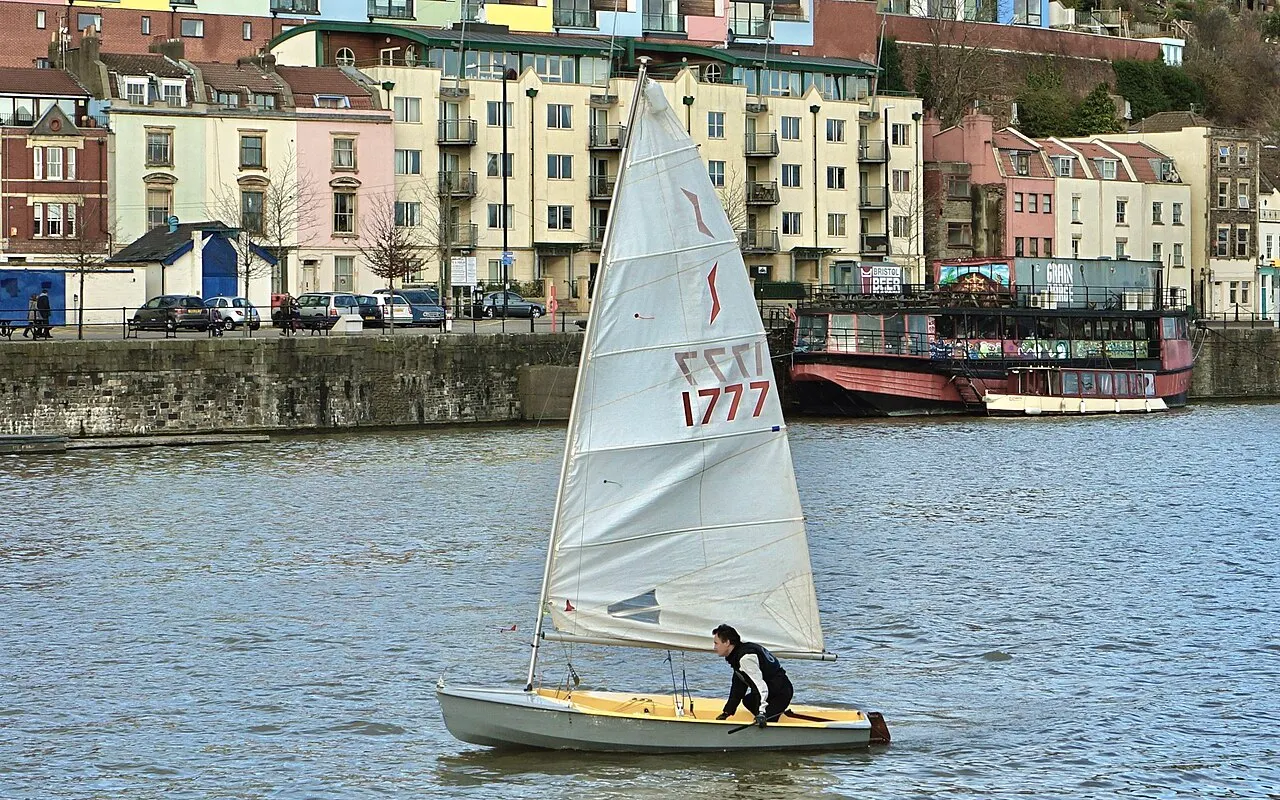 Un dériveur naviguant dans un port, grand-voile bien gonflée