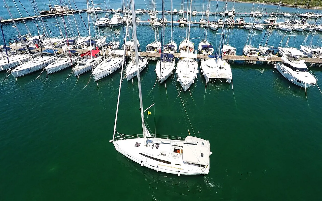 Vue aérienne d'un voilier quittant le port au moteur entre des rangées de yachts à quai