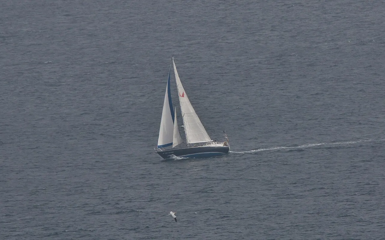 Un sloop qui file sur une mer grise en laissant un sillage