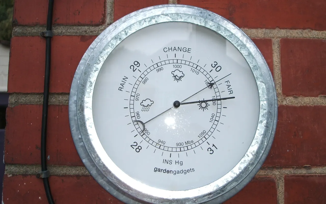 A round aneroid barometer mounted on a brick wall
