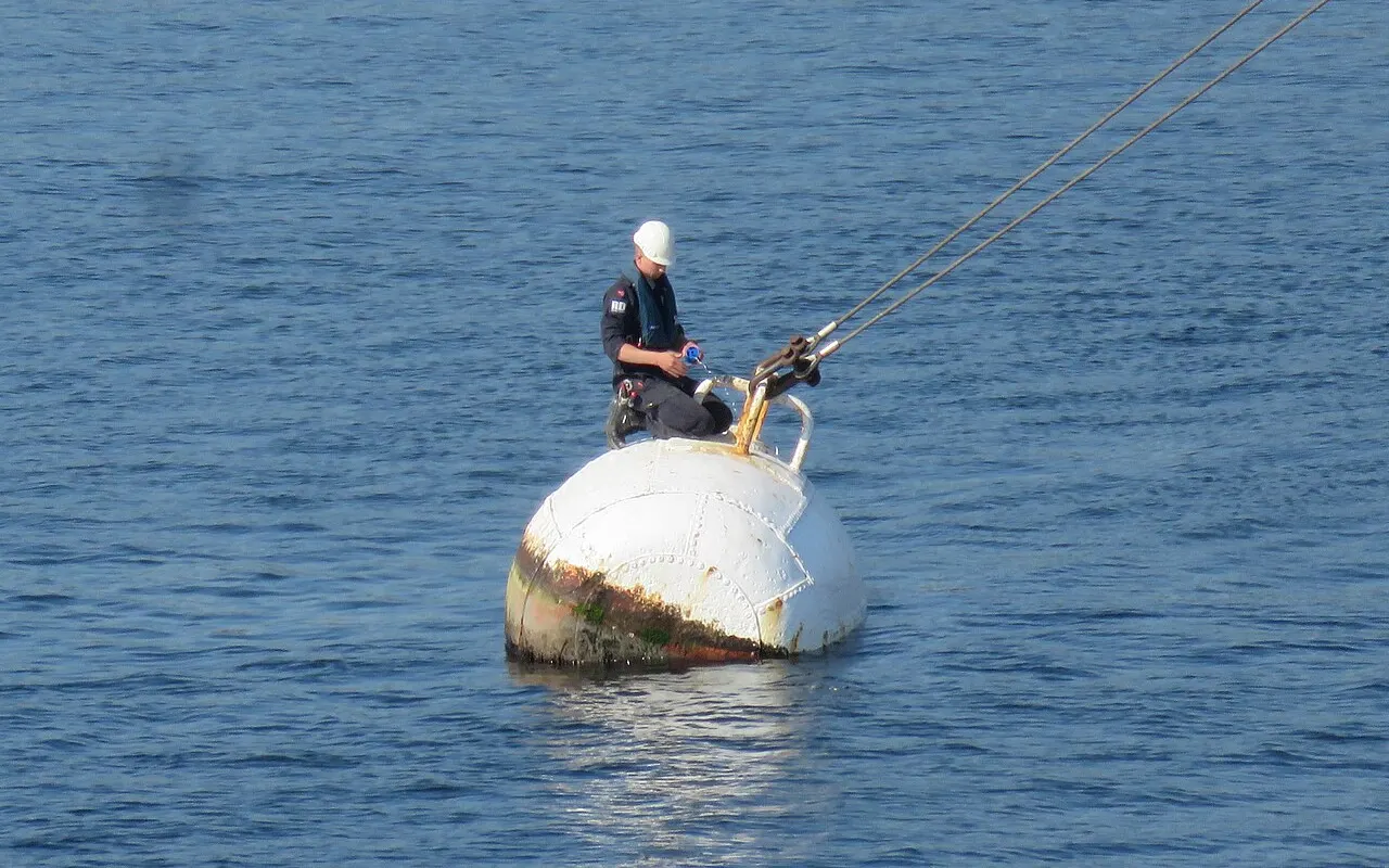 A sailor standing on a large mooring buoy securing a line