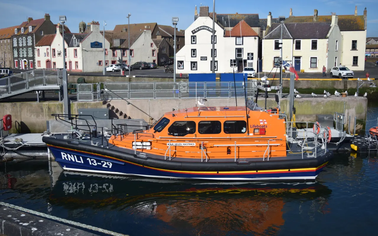 An orange and blue Shannon-class RNLI all-weather lifeboat moored in Eyemouth harbour