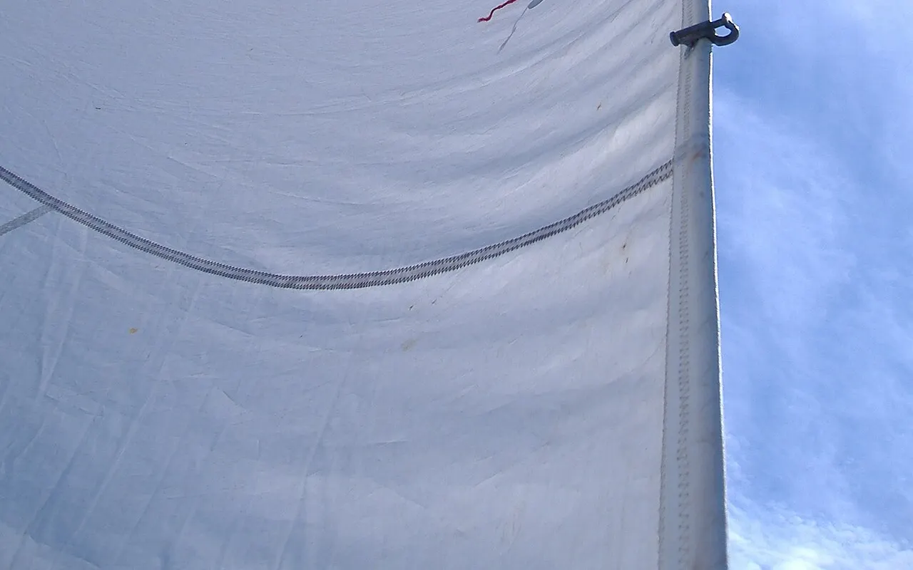 A red telltale streaming on a white jib, showing the airflow across the sail