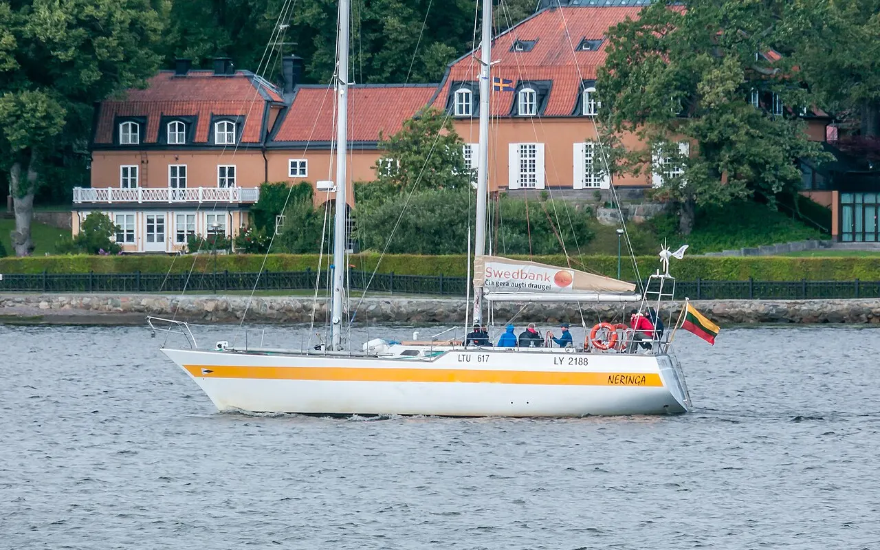 A two-masted schooner sailing past a waterfront