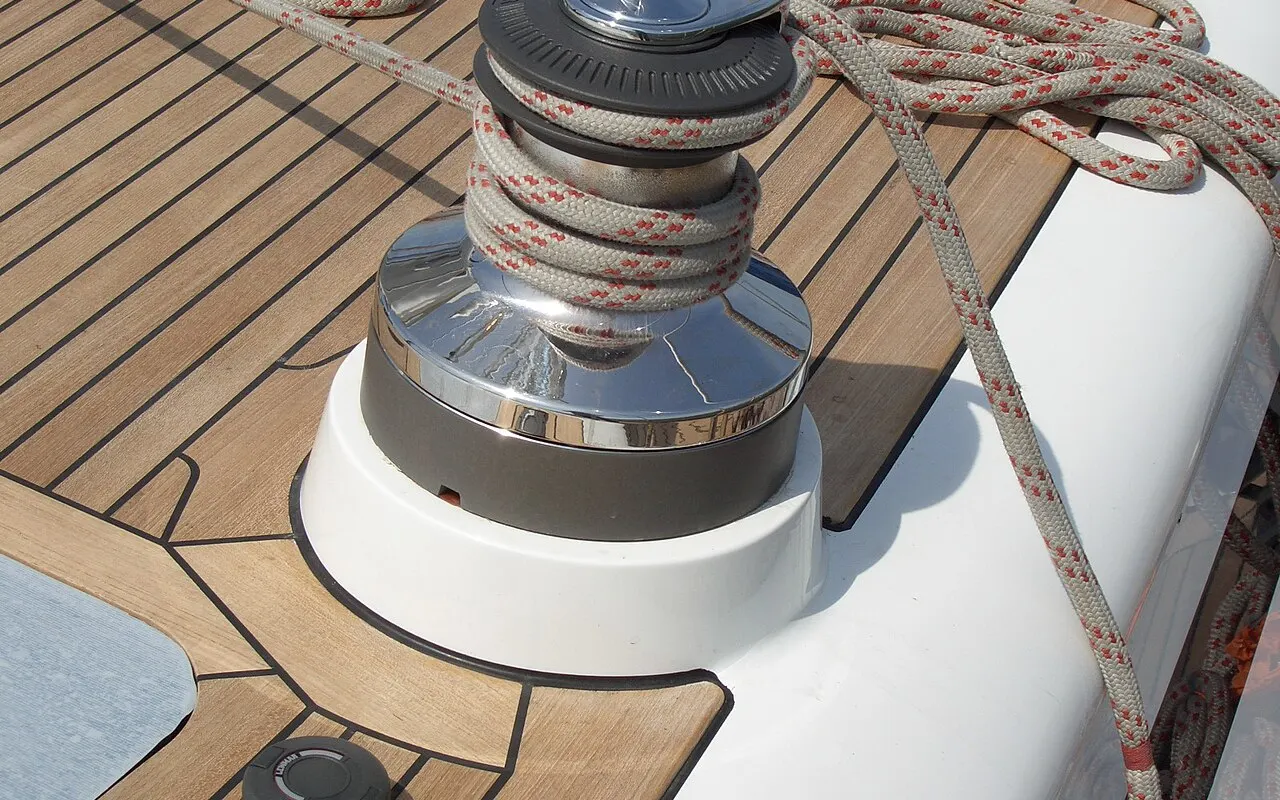 A chrome self-tailing winch on a teak deck with a sheet wrapped round it
