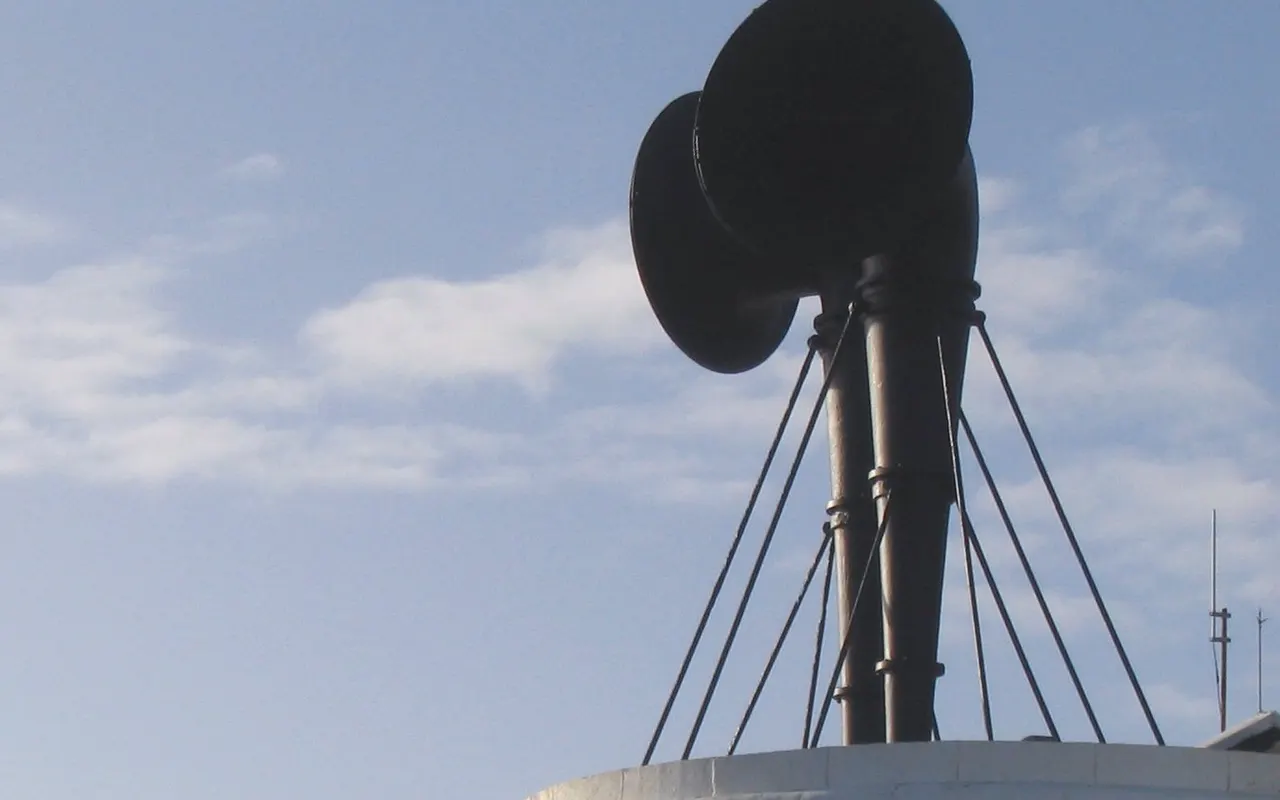 Two large ship's horns mounted on a mast against a blue sky