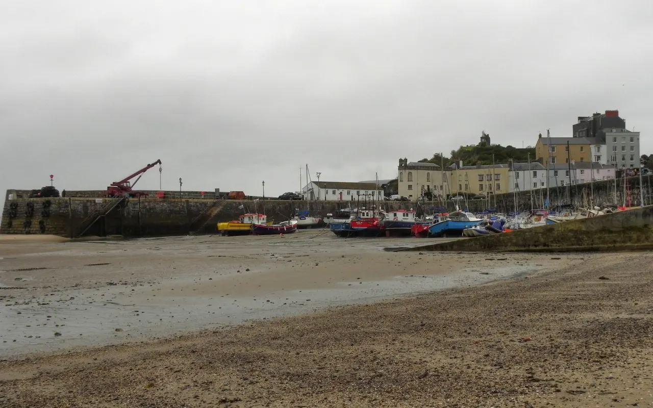 Tenby harbour at low tide, with boats sitting on the sand below the harbour wall