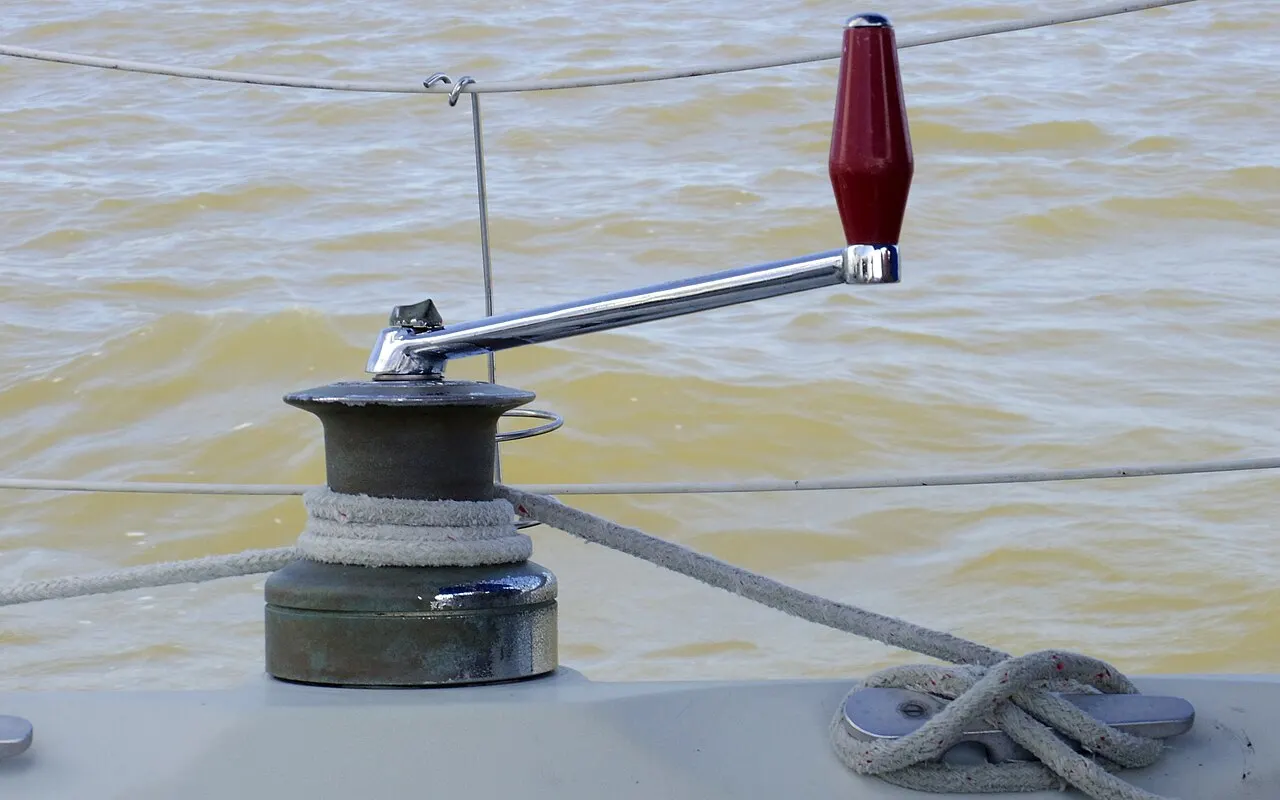 A winch with a red handle fitted and a sheet wrapped round the drum on a sailing yacht