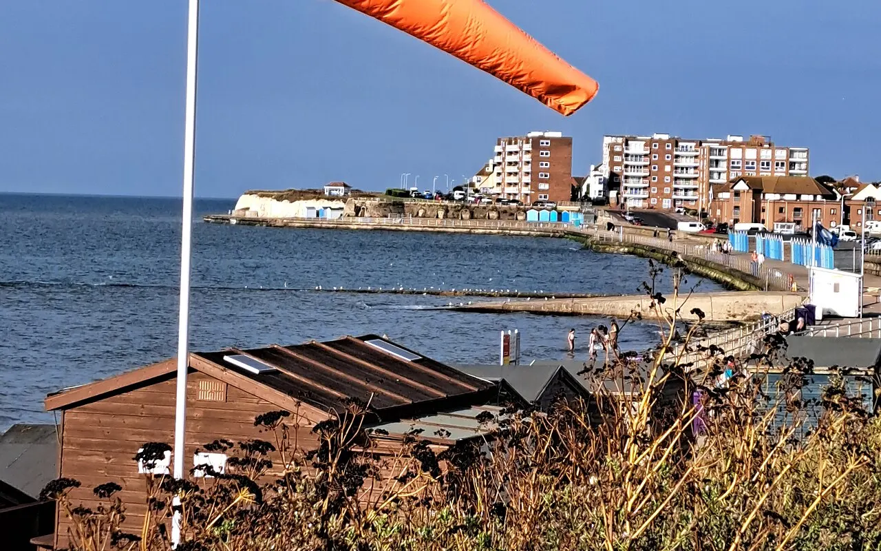 An orange windsock fully extended on a coastal pole, showing a fresh breeze