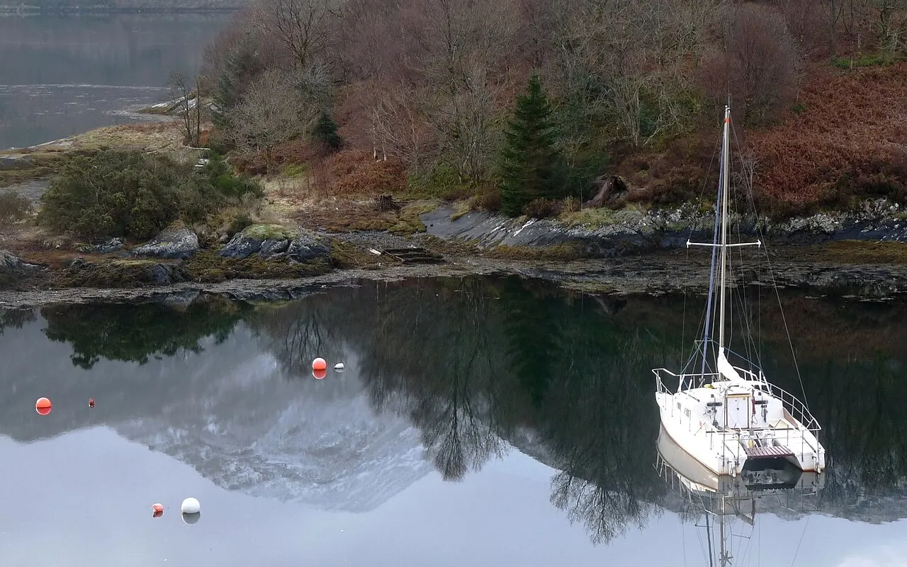 A white sailing yacht lying to a mooring in a calm Scottish loch
