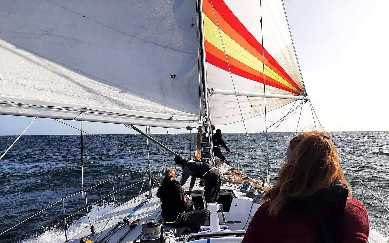 Crew sailing a yacht downwind under a red, yellow and white spinnaker