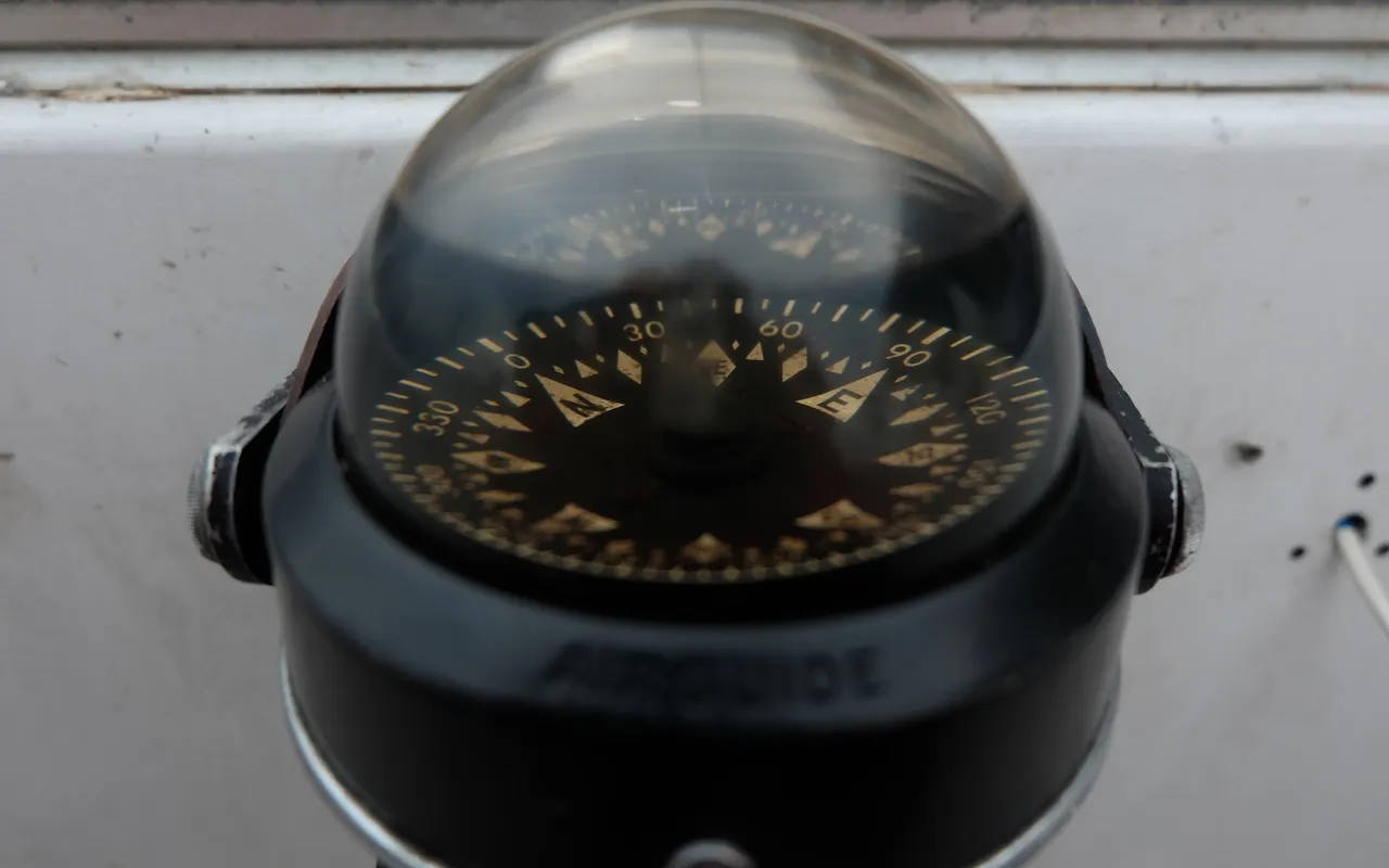 A domed steering compass mounted on a boat, its card showing degrees