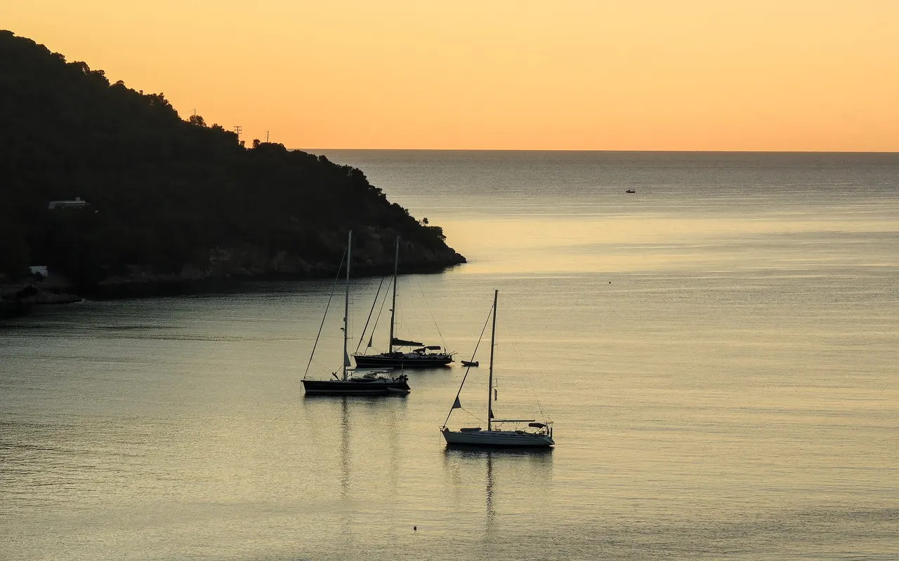 Three yachts at anchor in a calm, sheltered bay at dusk