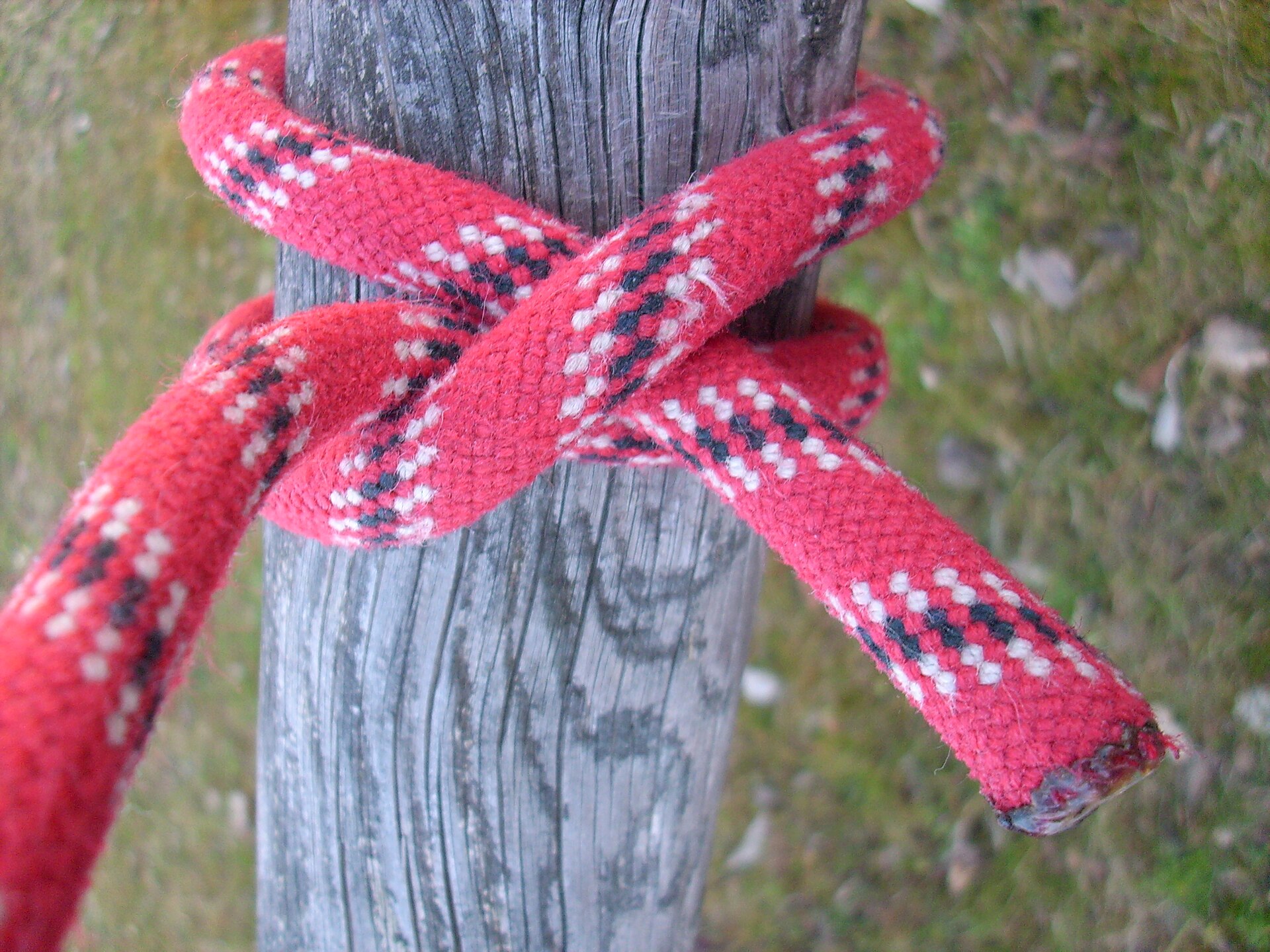 A clove hitch tied around a wooden post in red rope