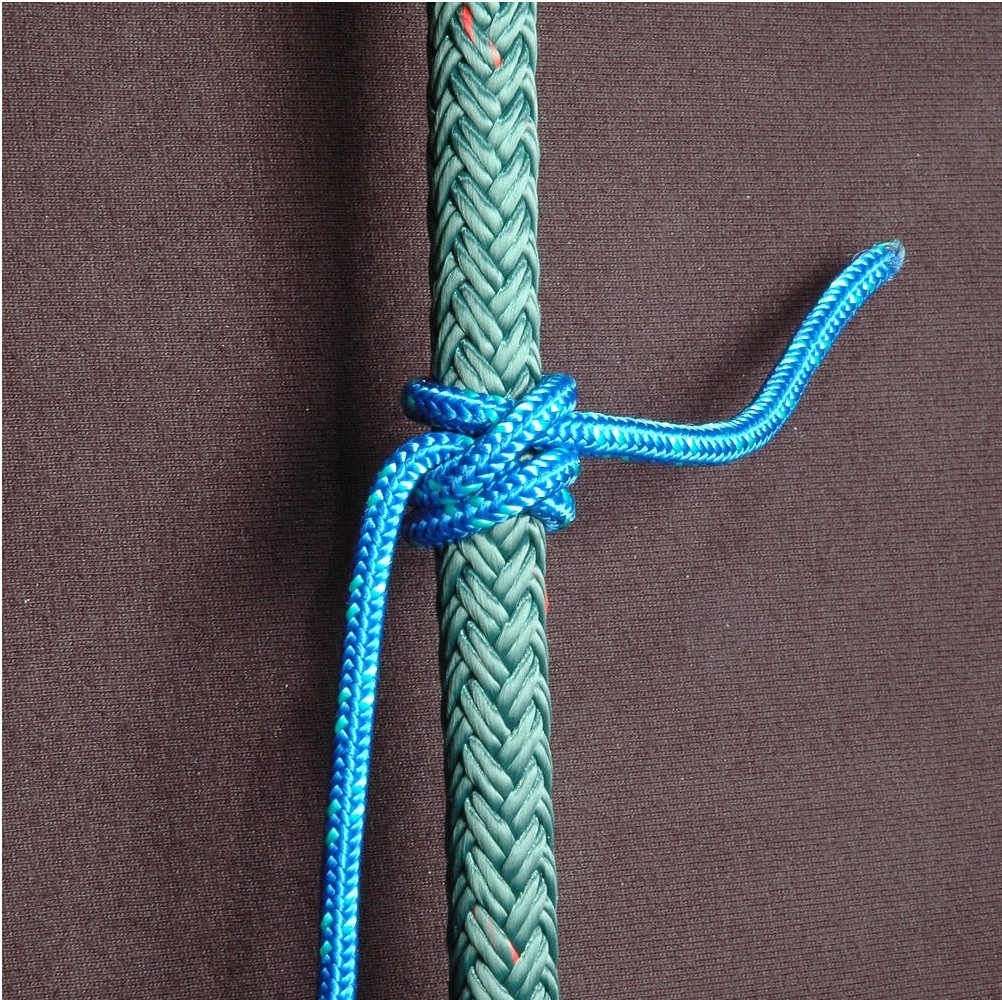 A rolling hitch in blue rope gripping a thicker green rope