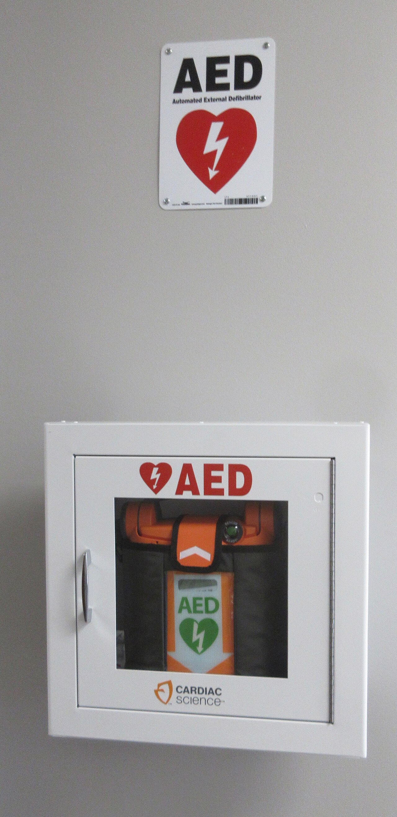 An automated external defibrillator in a wall compartment with a sign above