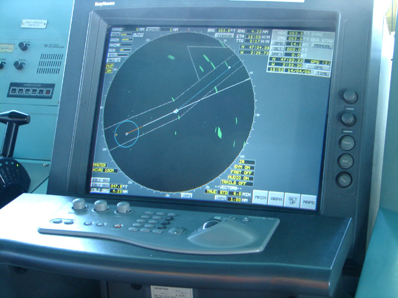 A marine radar display on a ship's bridge, showing the range rings, heading line, EBL and target echoes