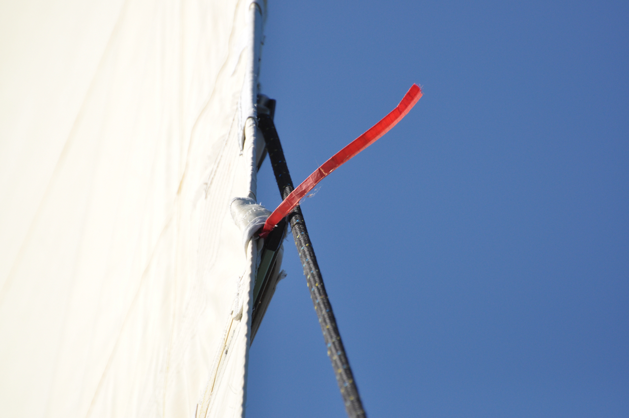 A red telltale streaming aft from the leech of a mainsail