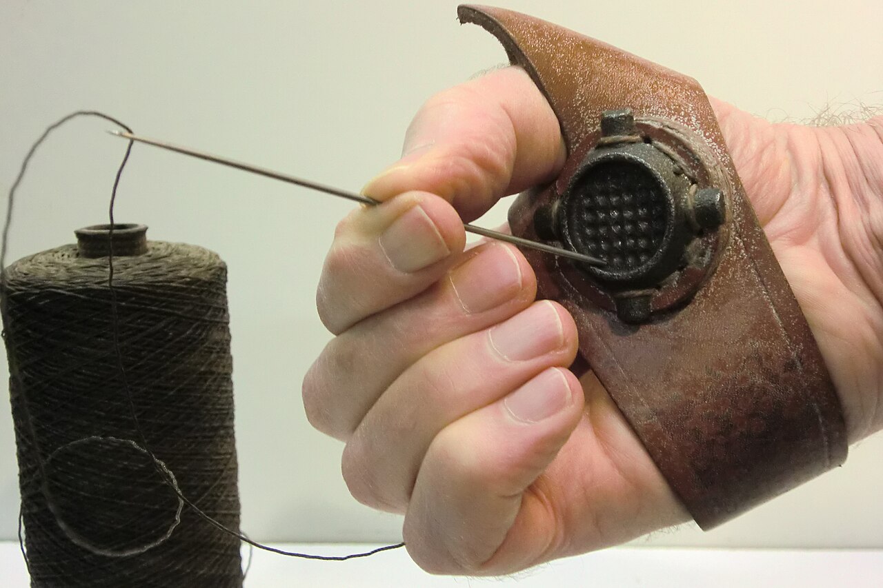A sailmaker's palm, needle and waxed thread, used for hand-sewing sail repairs