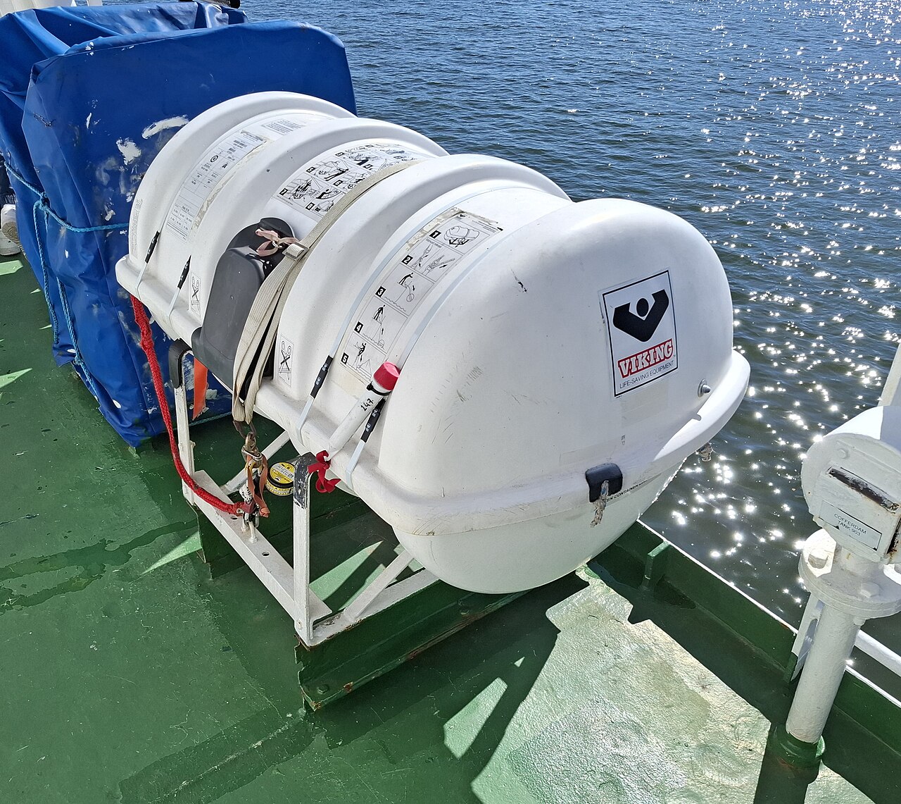 A Viking liferaft in a white glass-fibre canister on a cradle, with lashing, painter and instruction panels visible
